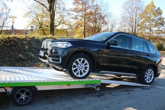 Ein schwarzes Auto fährt auf einen kippbaren Anhänger mit ausgefahrener Auffahrrampe auf